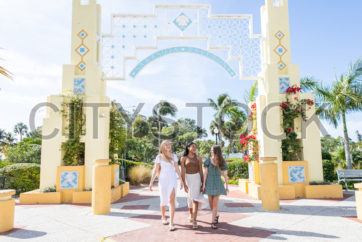 Three friends laughing and walking under Sarasota Bayfront arch