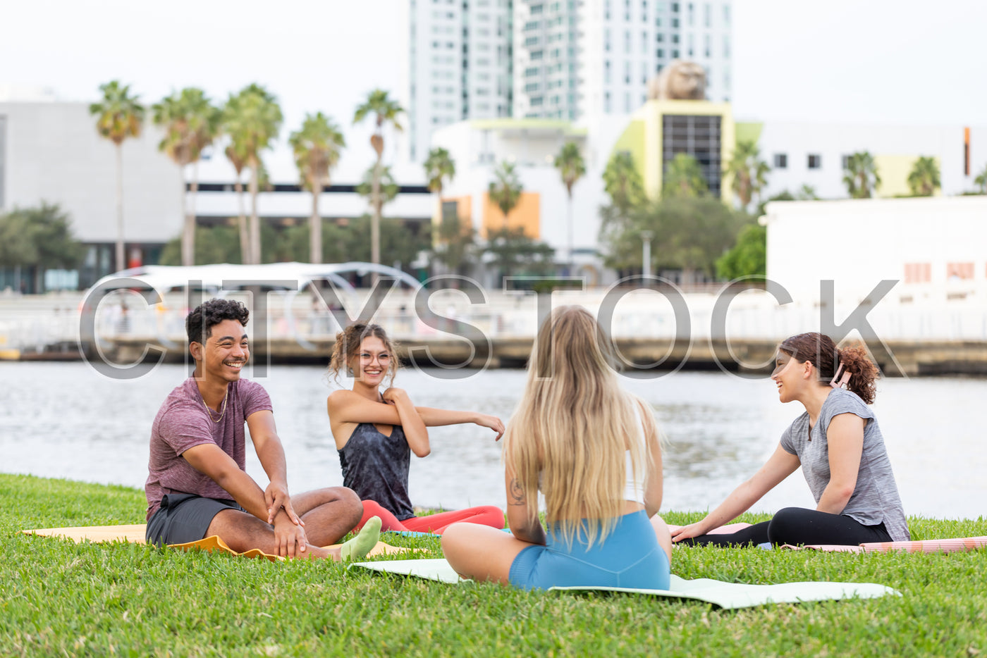 Young adults practicing yoga by Tampa river with city backdrop