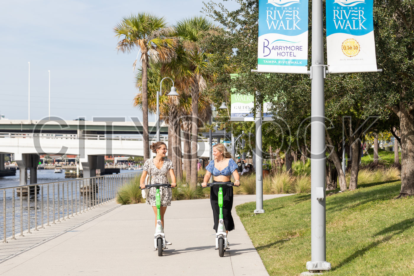 Young women enjoying a scooter ride on Tampa Riverwalk under sunny skies
