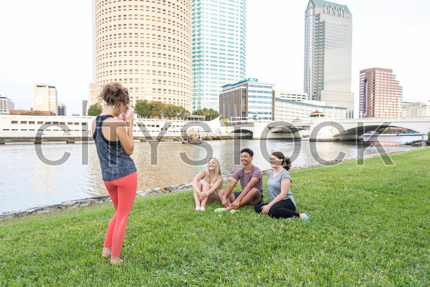 Group of diverse young friends sitting and standing in urban park, Tampa cityscape in background