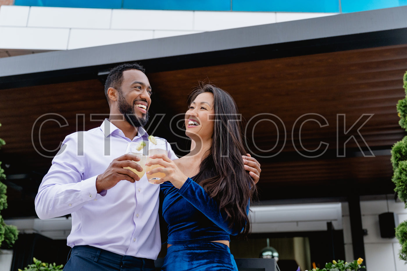 Joyful African American man and Asian woman toasting drinks