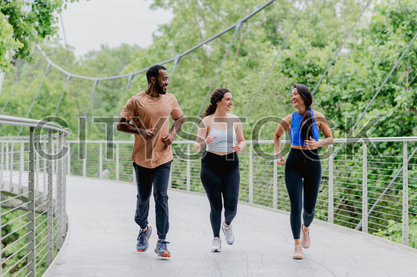 Diverse group of friends jogging and laughing on urban bridge