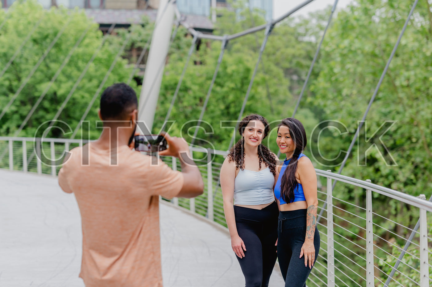 Two women posing happily during a fitness photoshoot on a bridge in Greenville