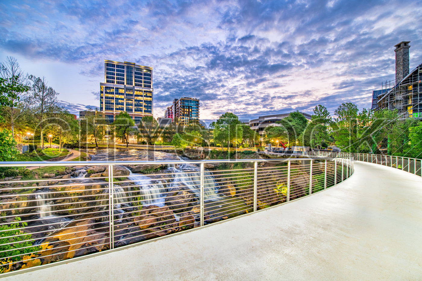 Modern Greenville, SC cityscape at twilight with waterfall and pedestrian bridge