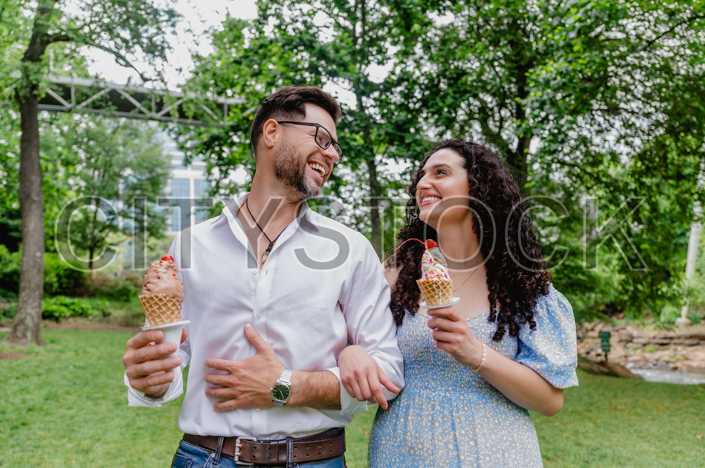 Couple laughing while holding ice cream cones in park