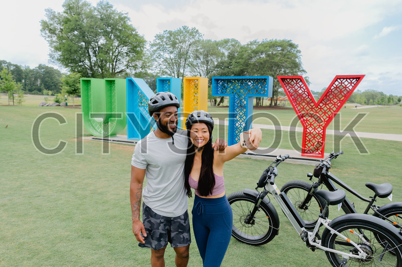 Smiling couple biking in Greenville park with UNITY sculpture
