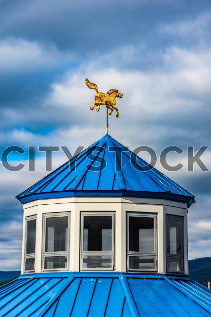 Golden horse weathervane on blue building rooftop against cloudy sky