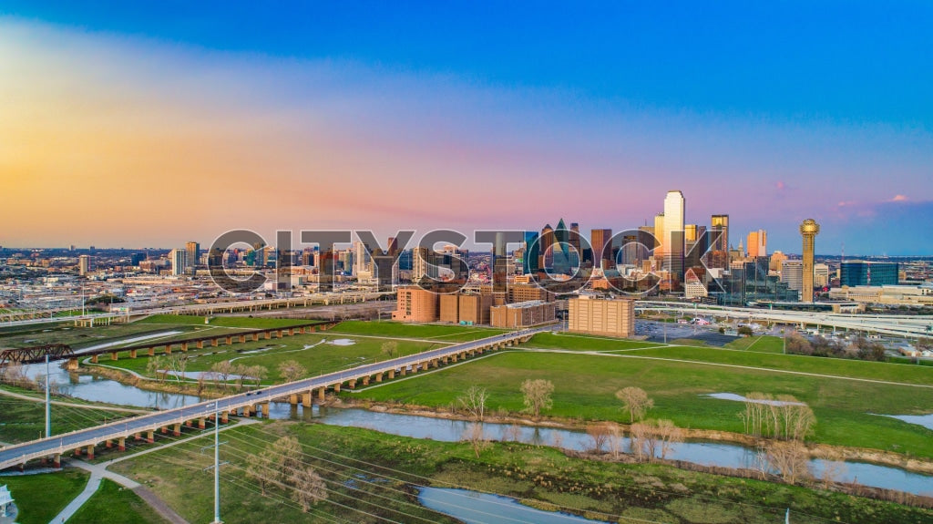 Dramatic sunset over Dallas cityscape with reflective waters and green spaces