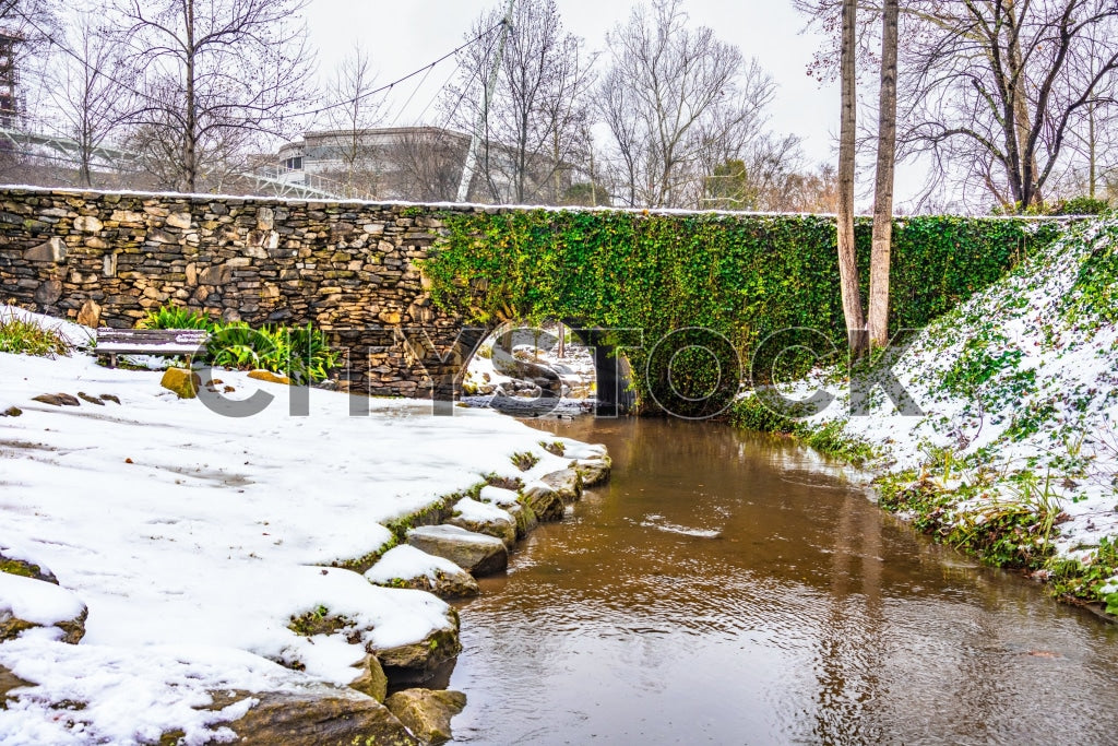 Snow covered urban creek with stone wall and green ivy in Greenville, SC