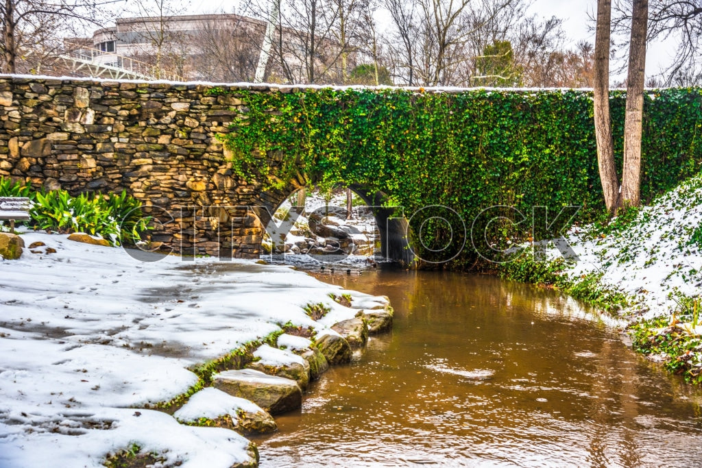Tranquil winter creek with snowy banks and ivy-covered stone wall in Greenville