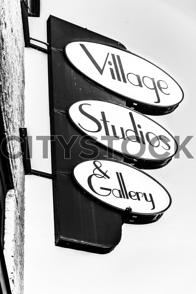 Black and white photo of overlapping Village Studio & Gallery signs on building