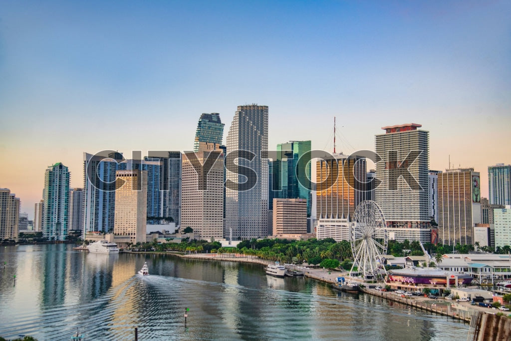Miami skyline at sunset featuring skyscrapers, a Ferris wheel, and boats on the water