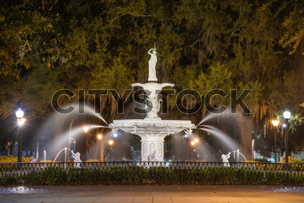Historic Savannah fountain illuminated at night with live oaks